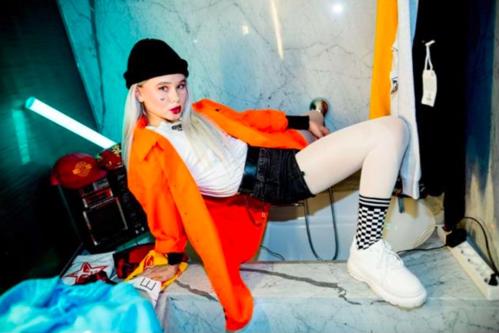 Guest in an orange jacket posing in a styled hotel room at Fashion Room Service